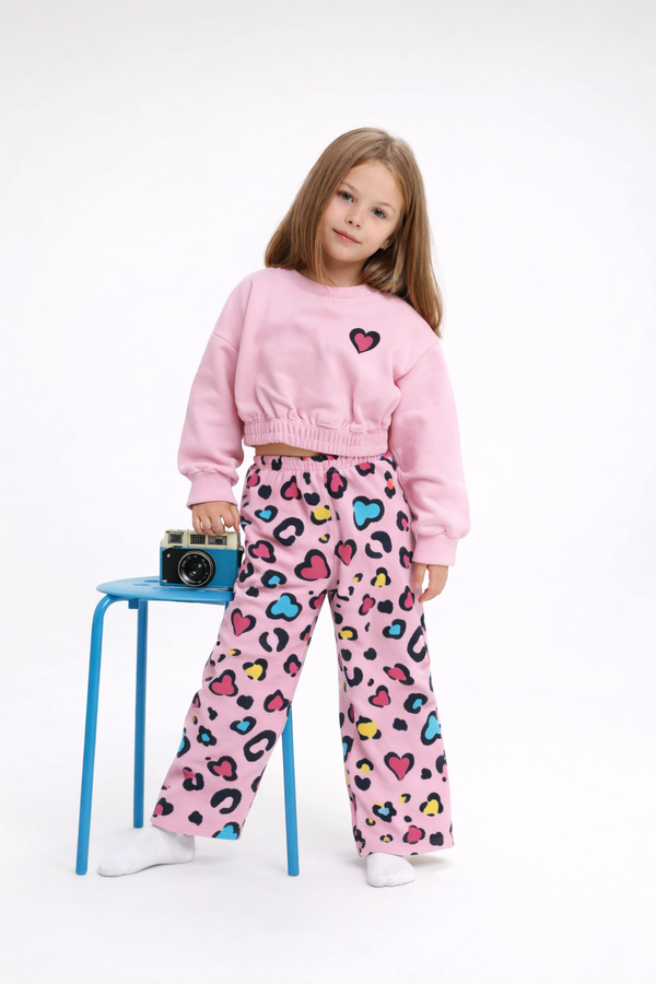 Child wearing a pink sweatshirt and colorful leopard print pants, standing next to a blue stool with a camera on it.