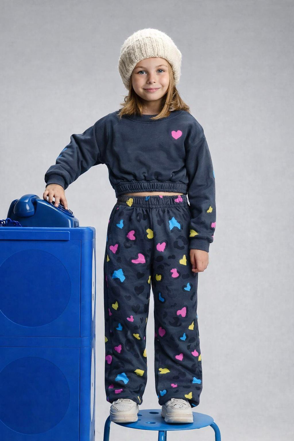 Child wearing a navy sweater and colorful pants standing next to a blue object on a gray background